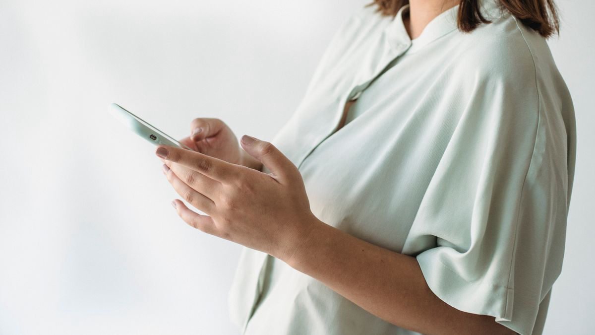 Woman in a light shirt checking her smartphone indoors