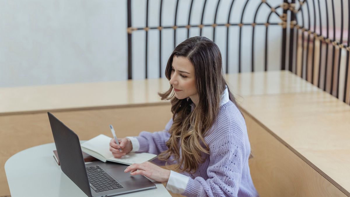 A woman sitting at a table and reading carefully on her laptop