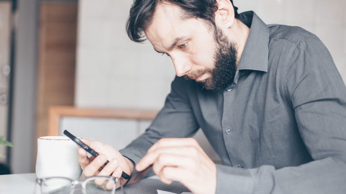 Bearded man looking closely at his smartphone, deep in thought