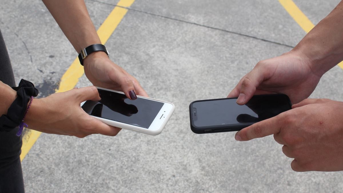 Two people holding their smartphones side by side outdoors