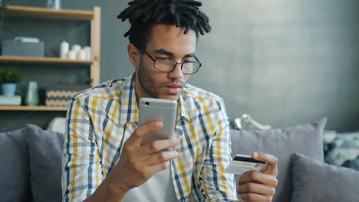 Young man shopping online with a smartphone and a bank card in his living room
