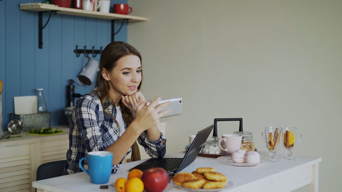Young woman using her phone and laptop over breakfast