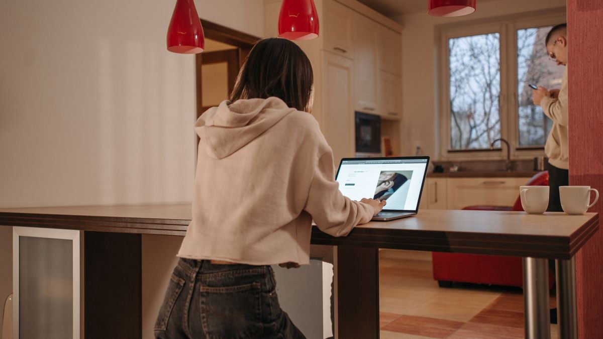 Woman in a hoodie working on a laptop at a kitchen counter