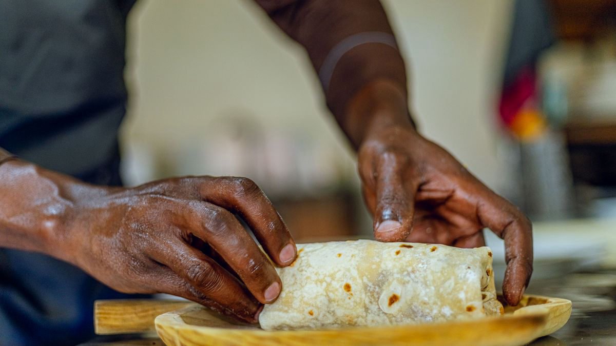 Hands wrapping a burrito on a wooden board in a kitchen