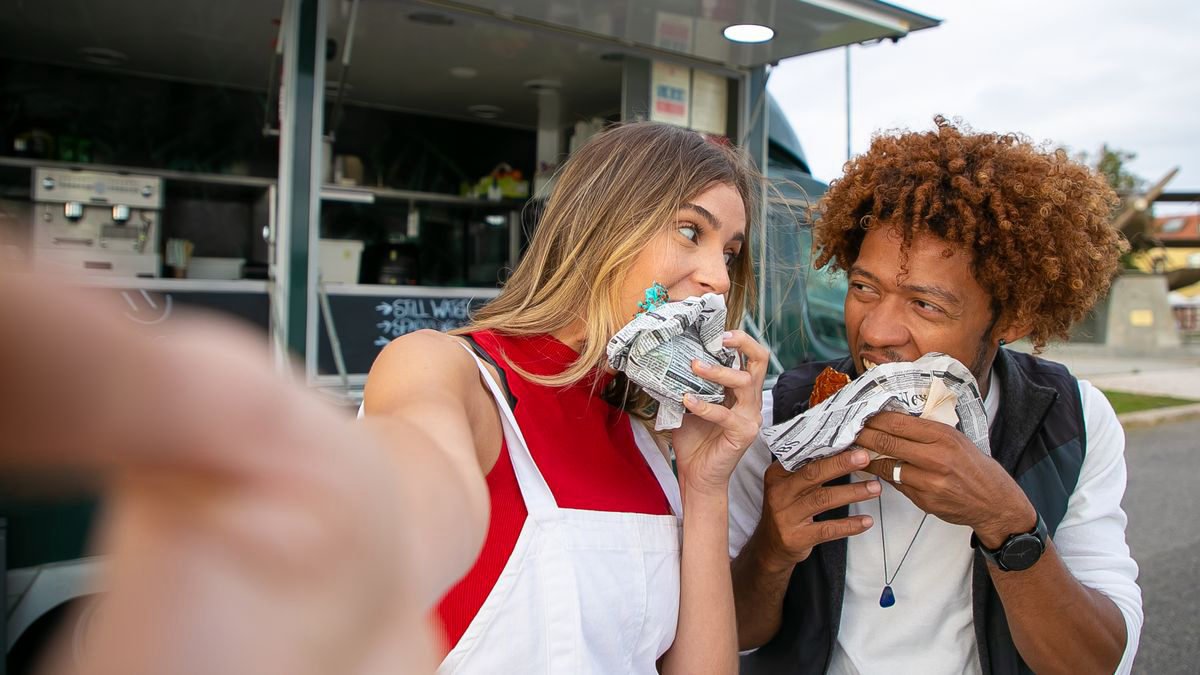 Two friends smiling and eating in front of a street food truck