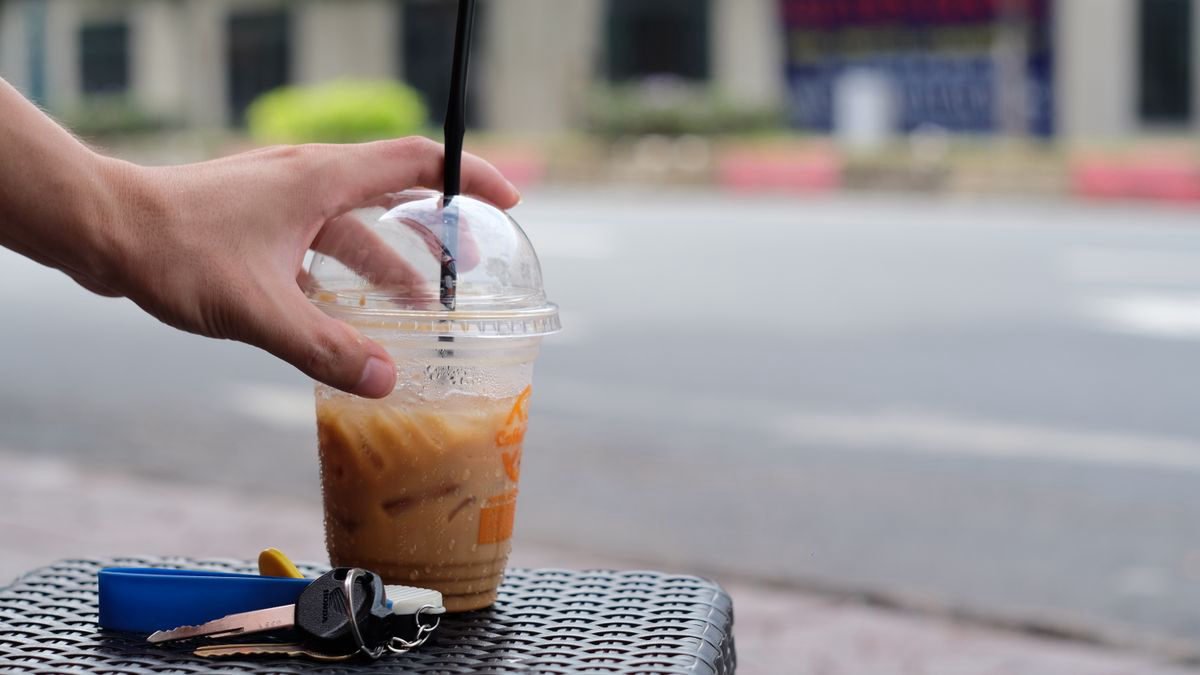 A hand holding an iced coffee cup on an outdoor table with keys nearby