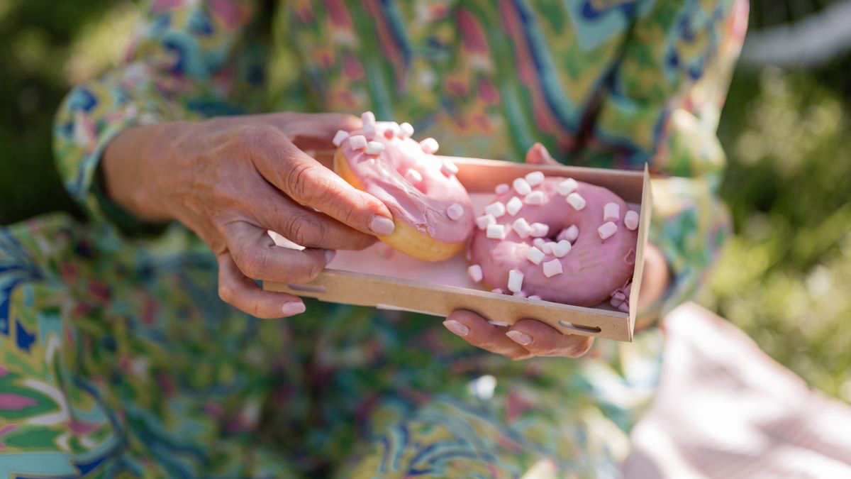 A woman holding two pink donuts at an outdoor picnic