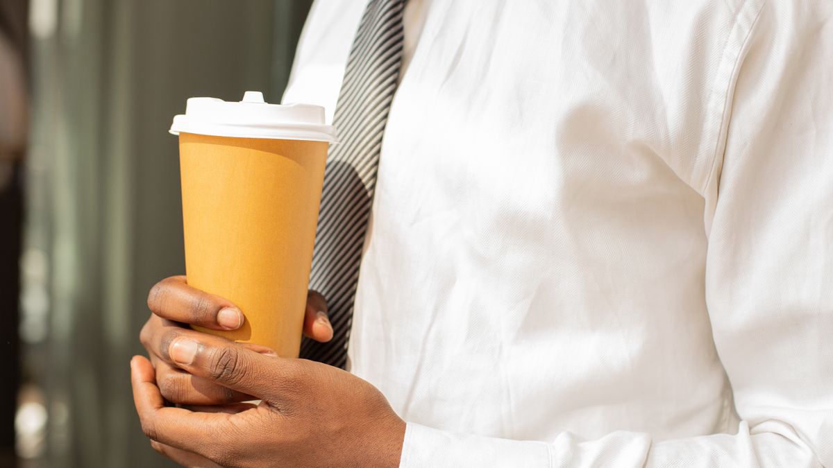 A man in a suit holding a disposable coffee cup outdoors on his way to work