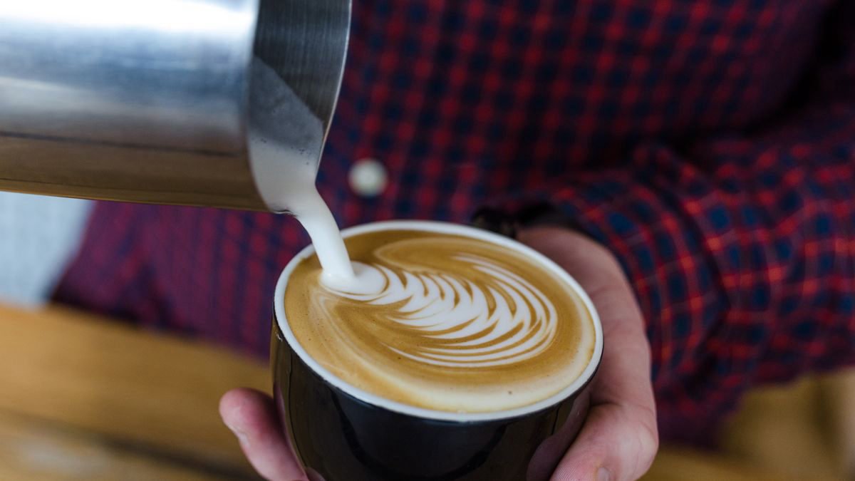A barista pouring latte art into a coffee cup
