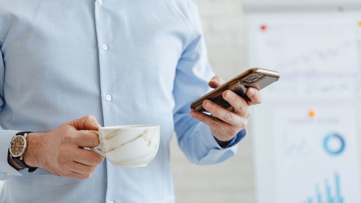 A man in a shirt holding a coffee cup while checking his phone