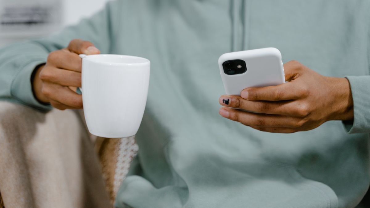 A person in a hoodie holding a coffee cup while using a smartphone