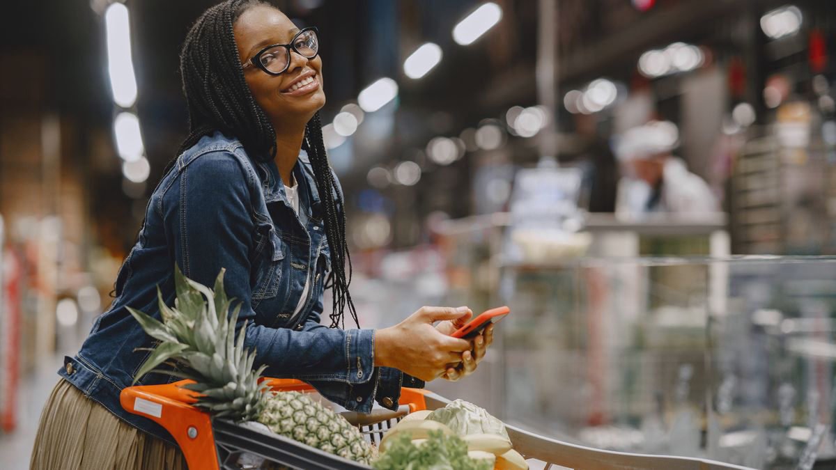 Smiling woman with a smartphone pushing a cart through a supermarket aisle