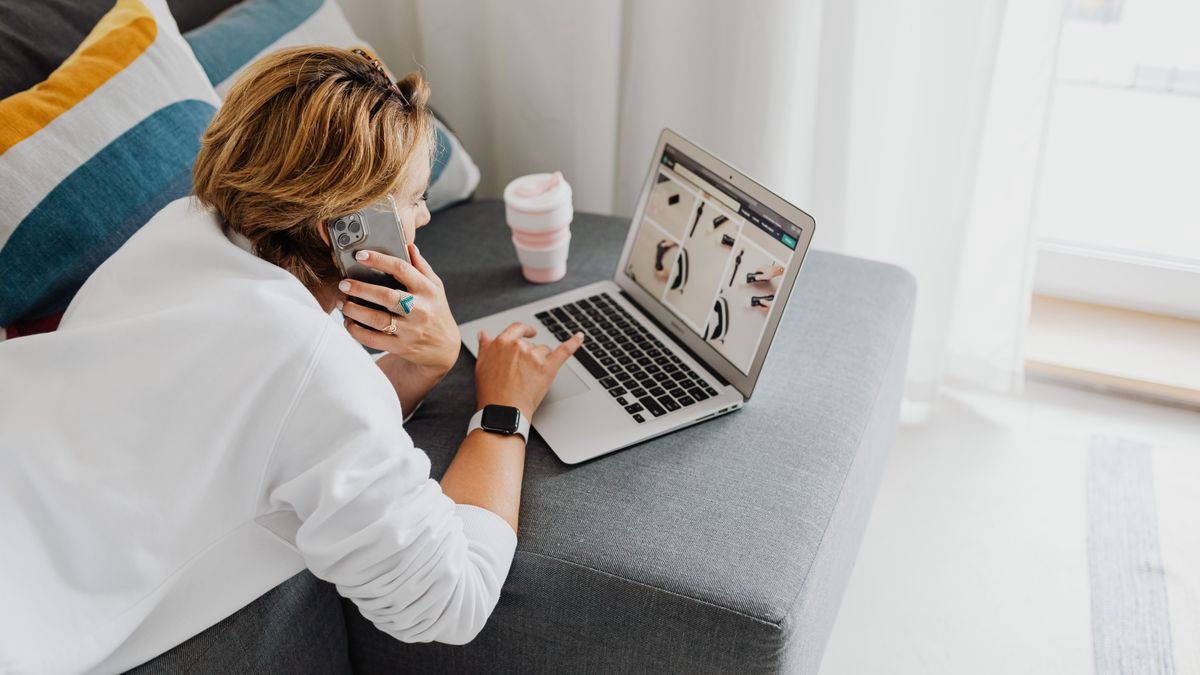 Woman lying on a sofa using a phone and a laptop at the same time