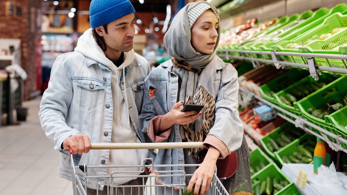 Couple choosing vegetables in a supermarket while checking a phone