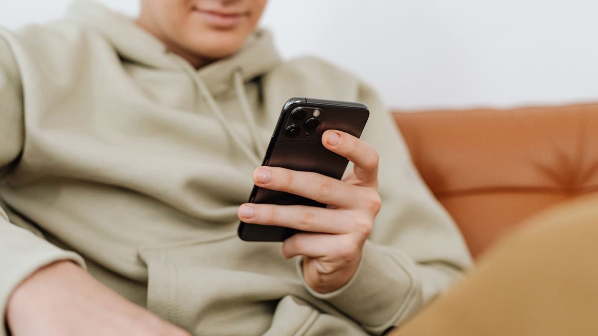 Young adult in a hoodie using a smartphone on a couch