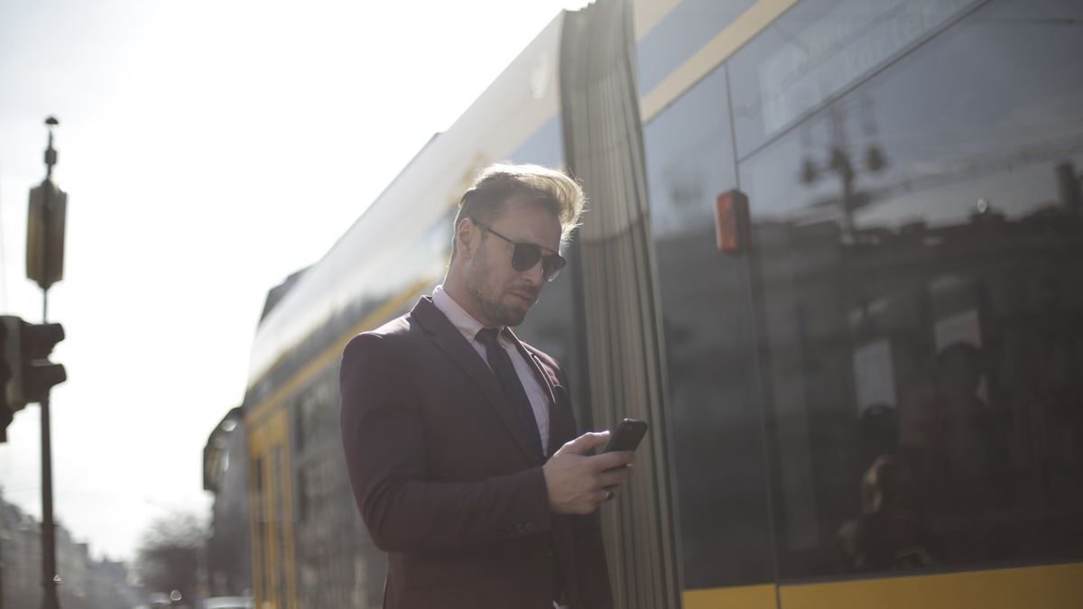 A man checking his phone on a sunny train platform