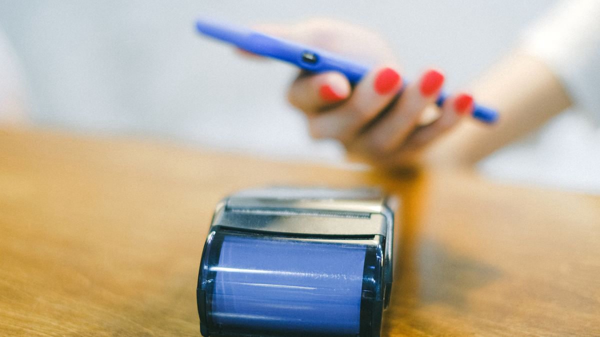 A close-up of a hand holding a smartphone to pay at a card terminal