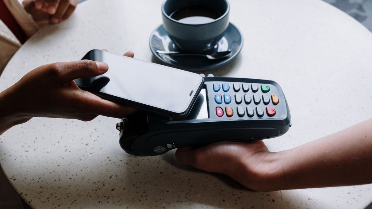 A person paying with a smartphone at a card reader on a shop counter
