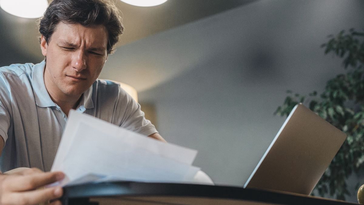 A man reviewing documents at a desk next to an open laptop