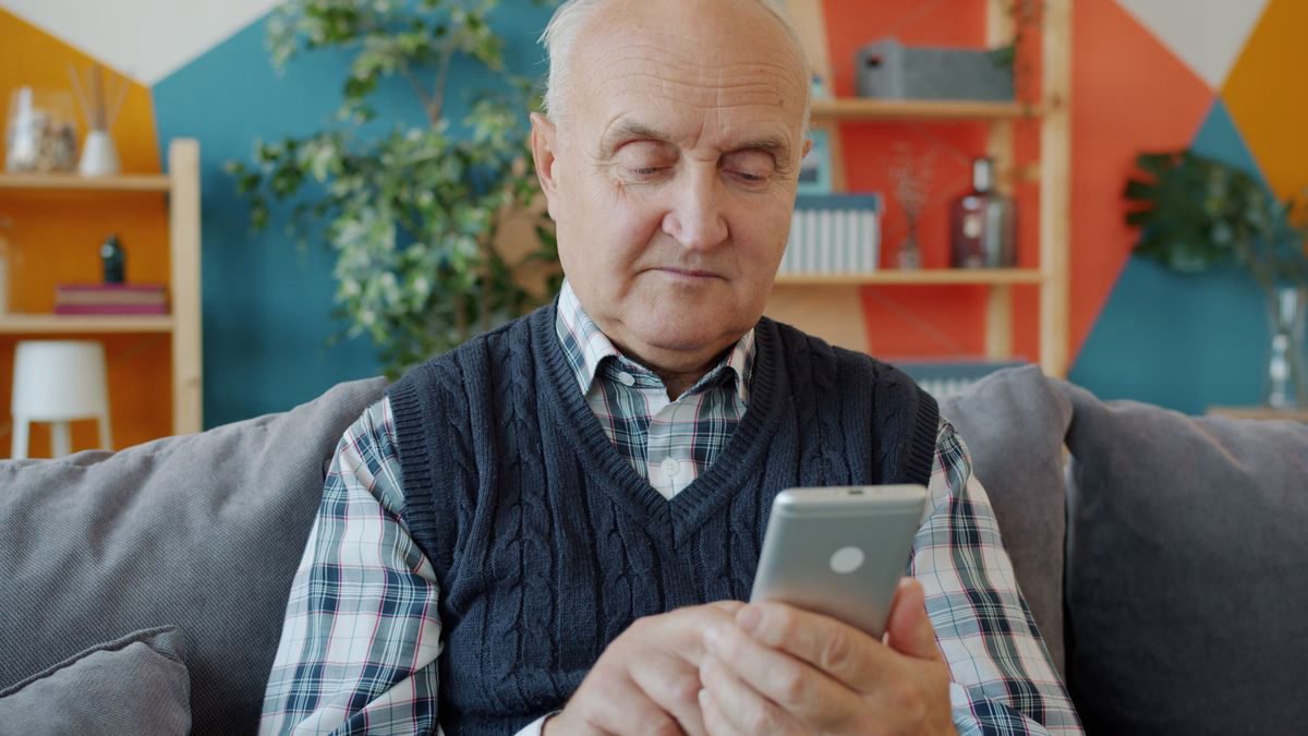 Elderly man using a smartphone while seated on a cosy sofa