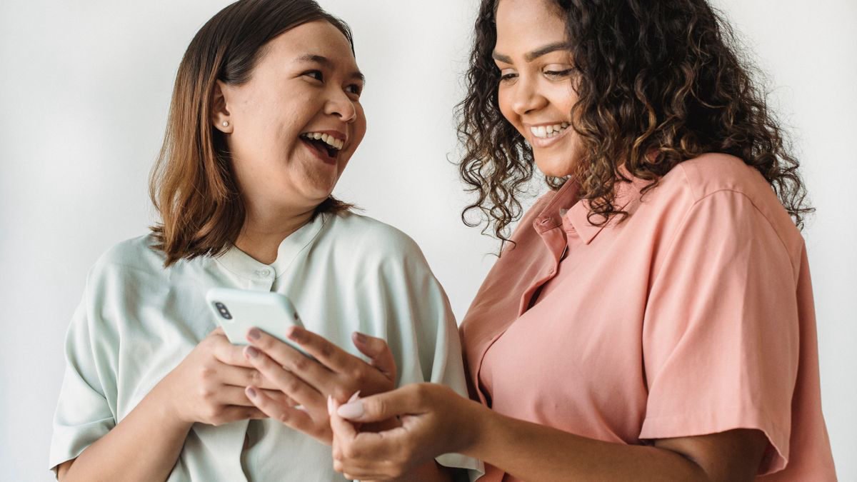 Two friends smiling while looking at a smartphone together