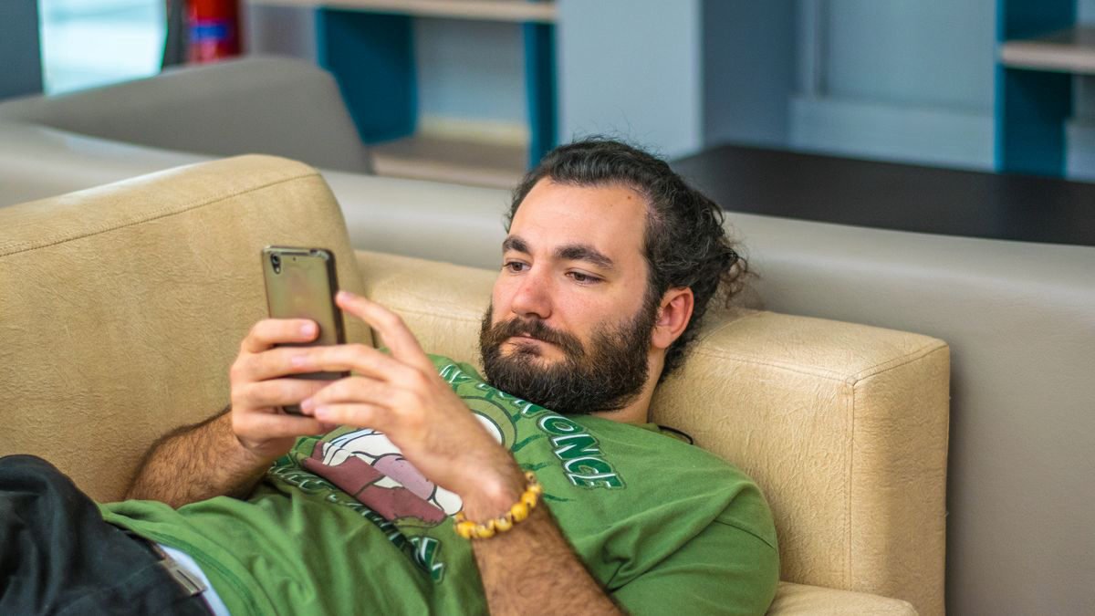 Bearded man lying on a sofa looking at his smartphone