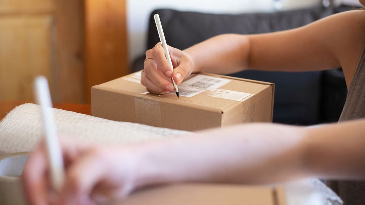Hands labelling a cardboard box for online shipping in a home office