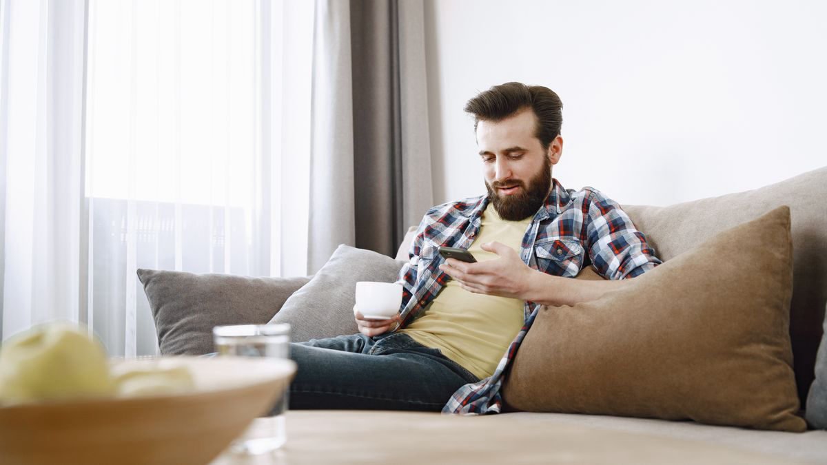 Man relaxing on a sofa with a coffee, using his smartphone