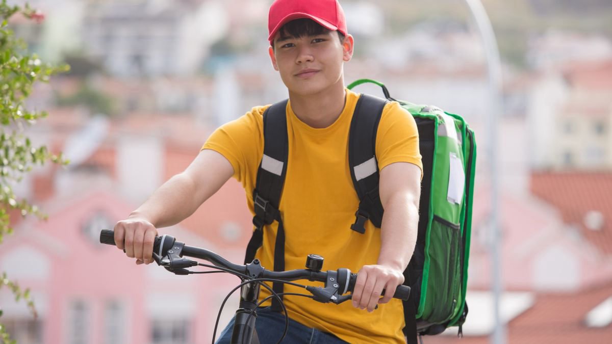Young man riding a bicycle with a food delivery bag through a city street