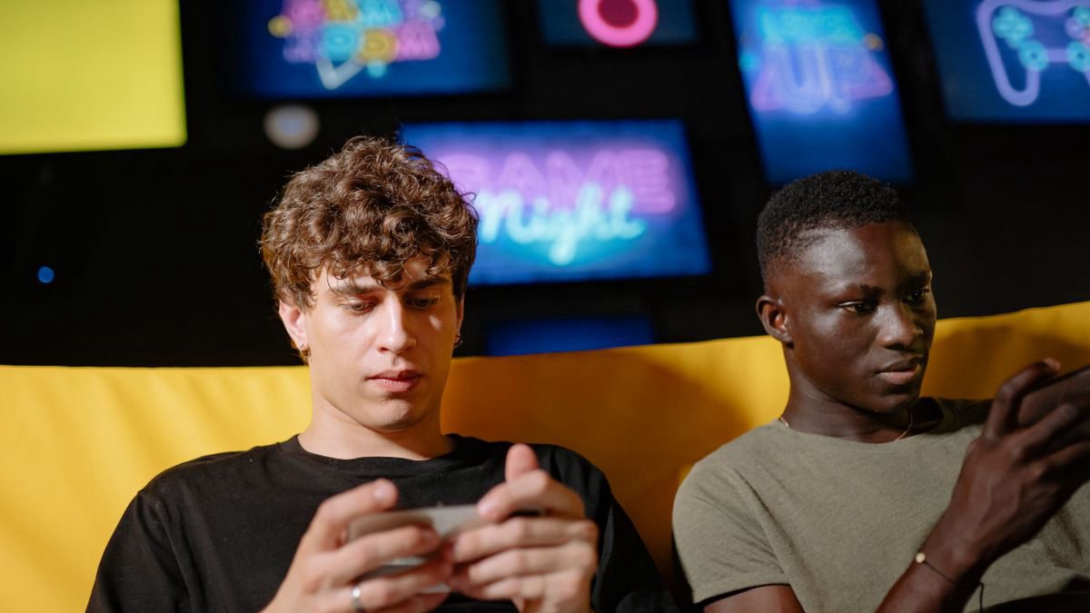 Two friends playing mobile games indoors, focused on their phones