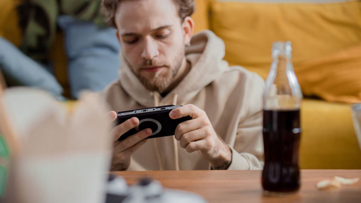 Young man focused on a mobile game while relaxing indoors with a drink