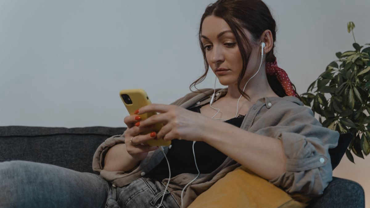 Woman relaxing on a couch with headphones watching her phone