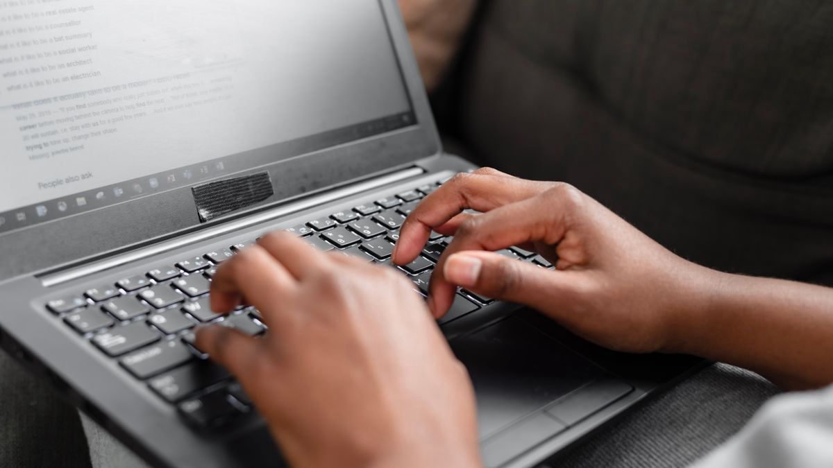 Hands typing on a laptop keyboard in a home setting