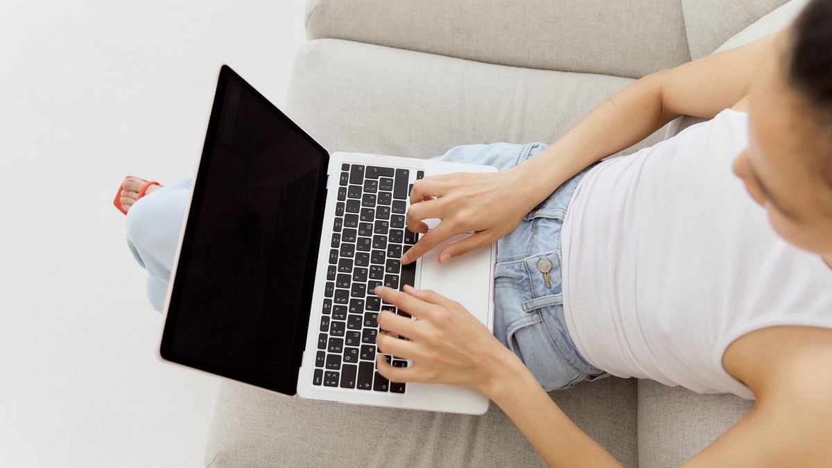Woman typing on a laptop while sitting on a comfortable sofa, seen from above