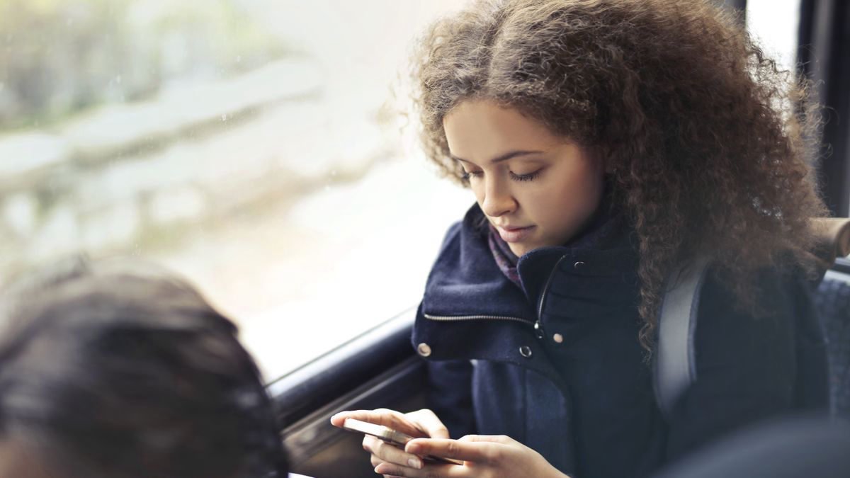 Young woman with curly hair texting on her smartphone on public transport