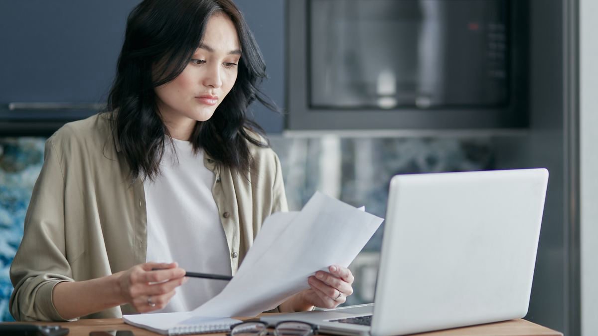 Woman reviewing documents while working on a laptop