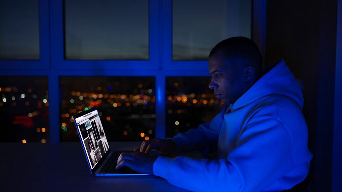 Man working on his laptop at night beside a window with city lights