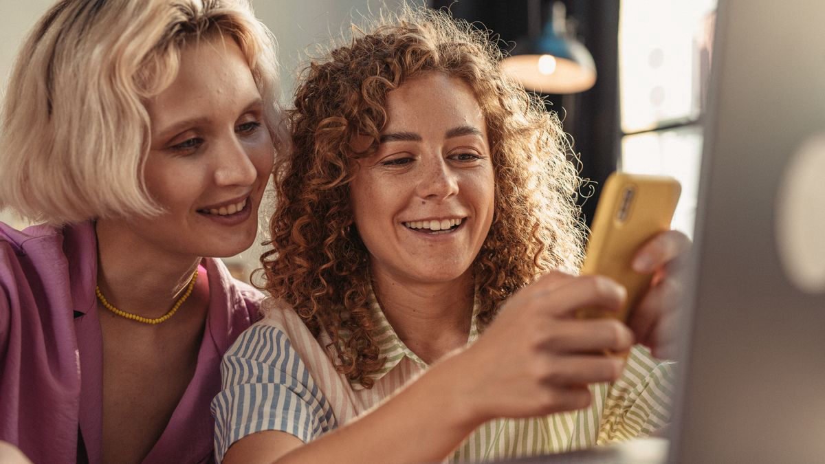 Two women smiling while looking at a smartphone together