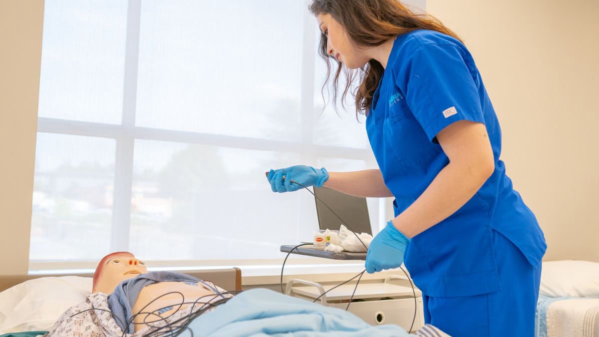 Nursing student in blue scrubs practicing on a training mannequin