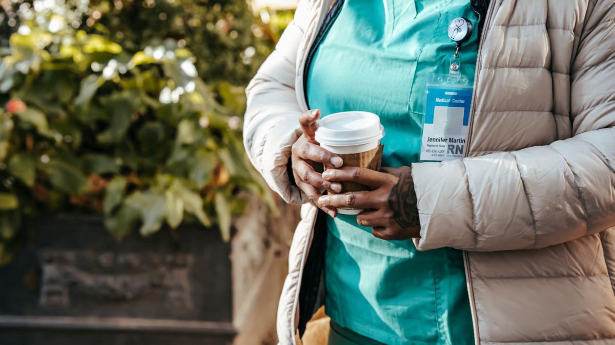 Nurse in a warm jacket holding a takeaway coffee outdoors