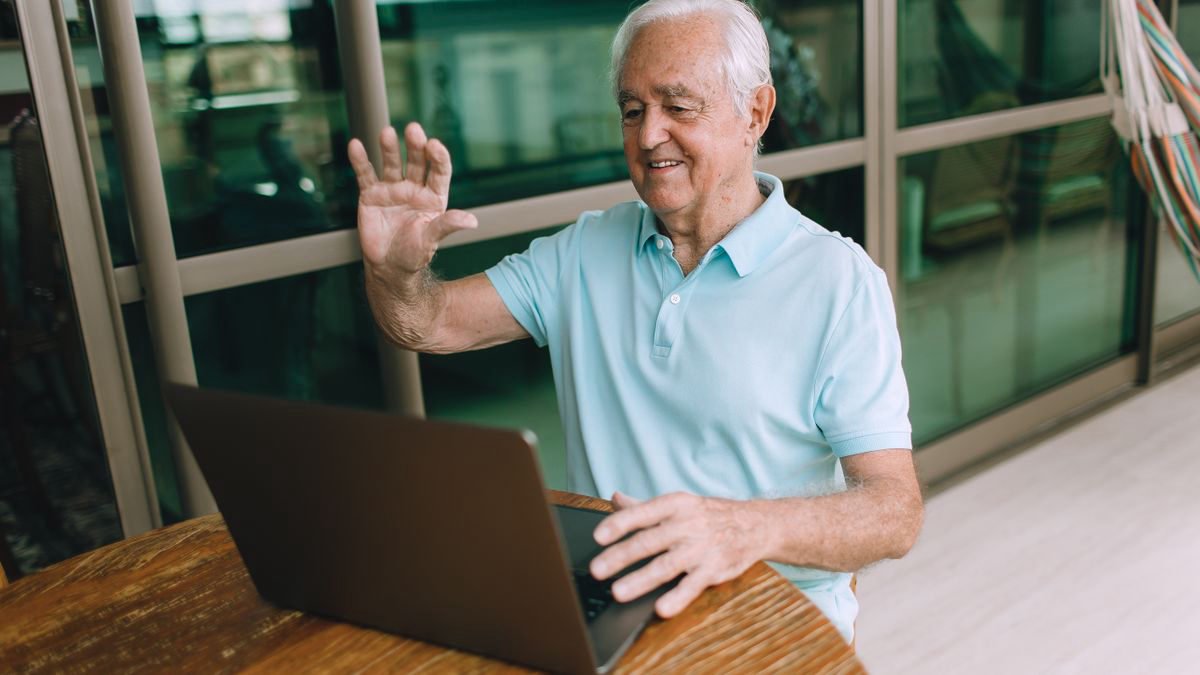 Elderly man smiling and waving during a video call on his laptop at home