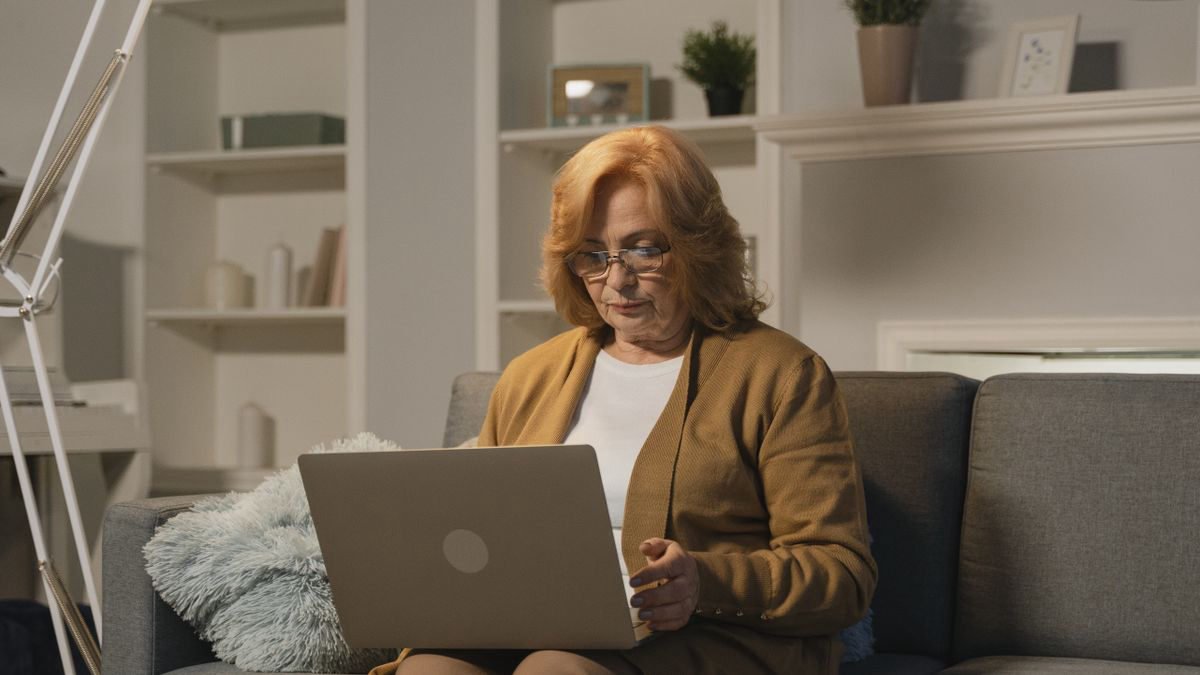 Senior woman with glasses working on a laptop in a cosy living room