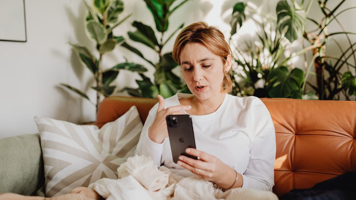 A woman in a white shirt using her smartphone on a sofa surrounded by plants