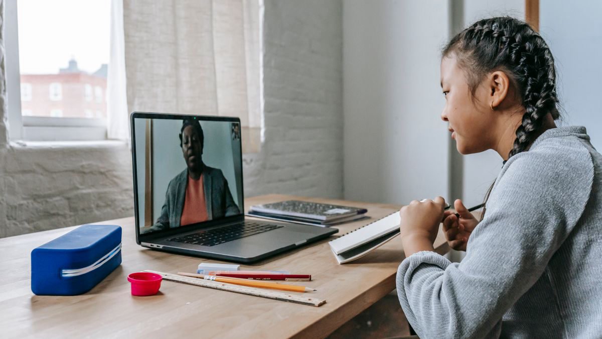 A girl at a laptop listening to a teacher explain a lesson over a video call