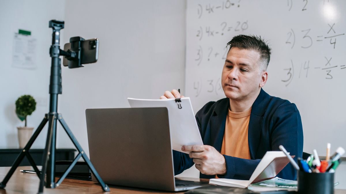 An educator recording an online lesson with a laptop and camera set up at home