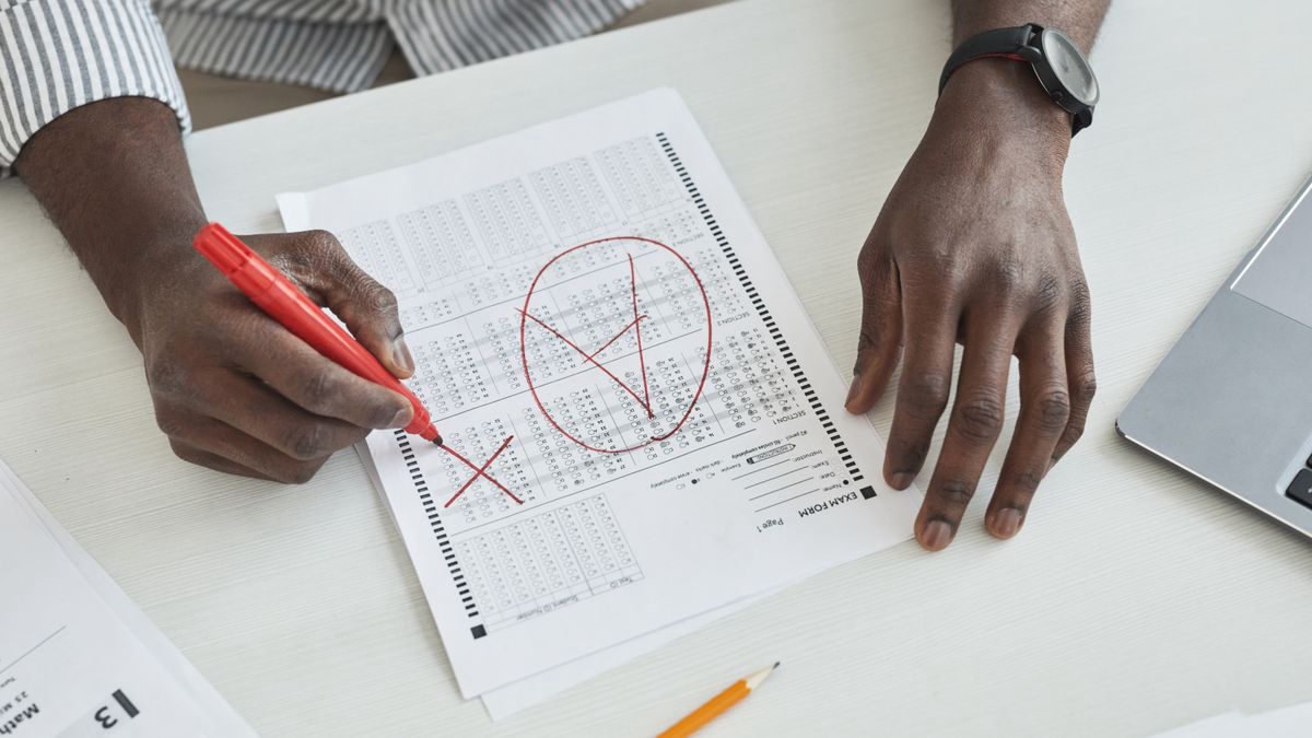Close-up of a teacher marking a test paper with a red marker at a desk