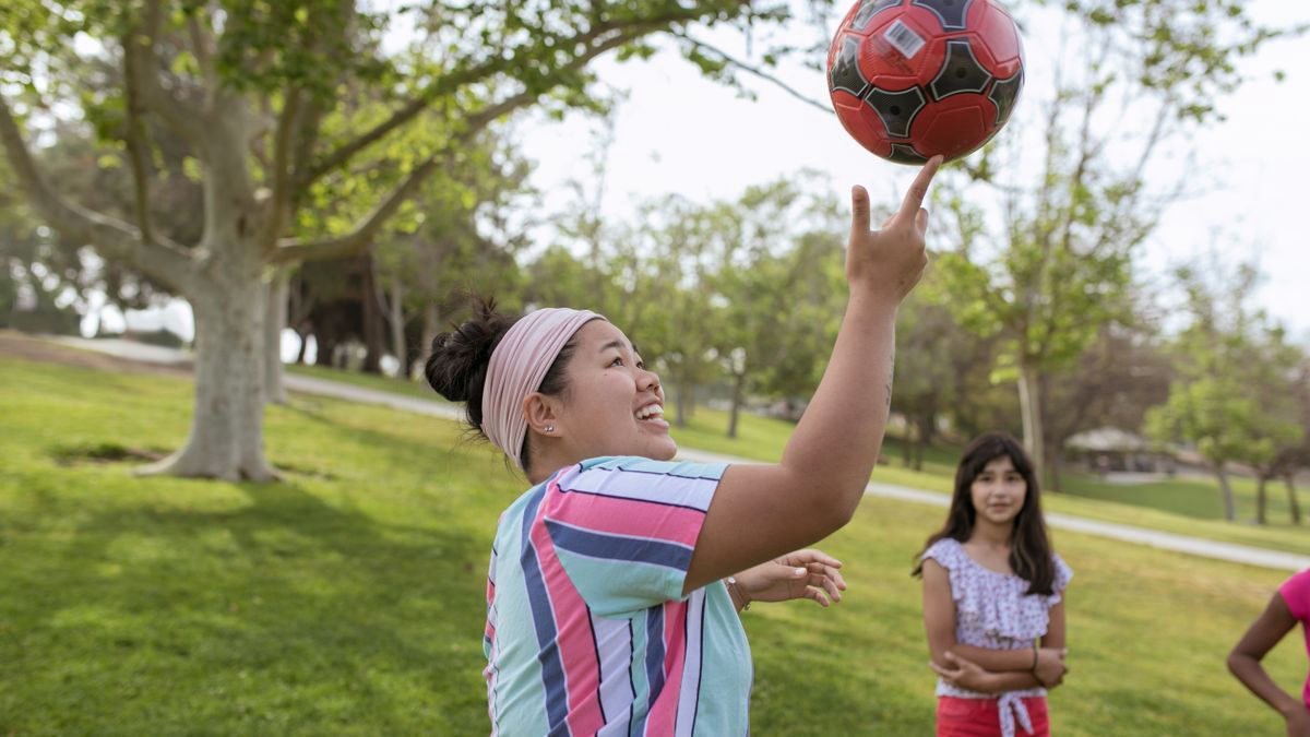 Children playing football in a sunny park during a summer camp