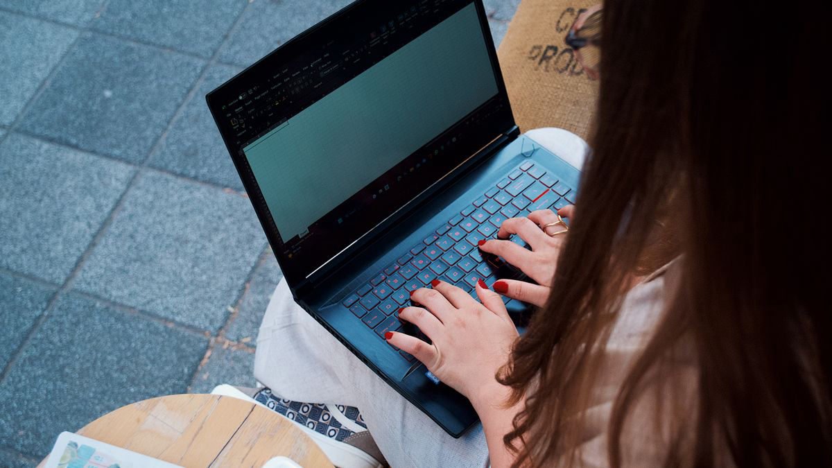 A young woman typing on a laptop at an outdoor cafe table