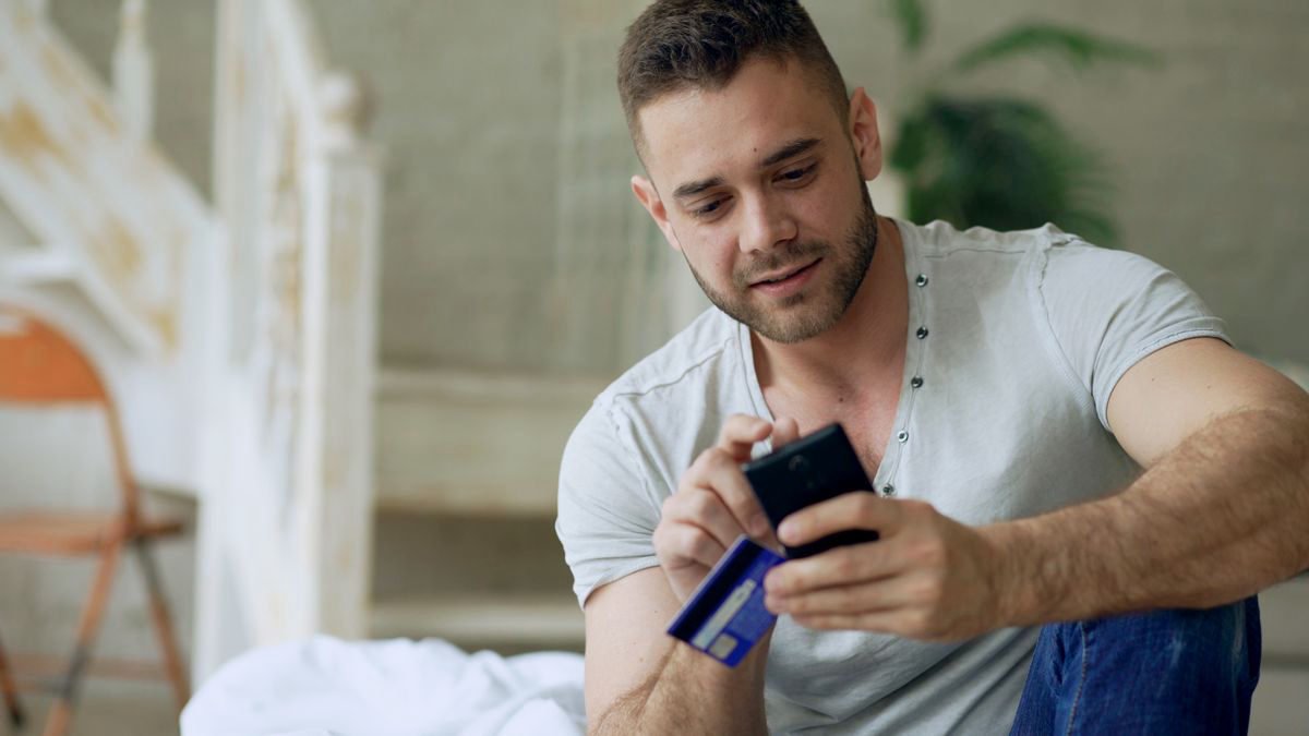 Young man using a smartphone and a bank card at home