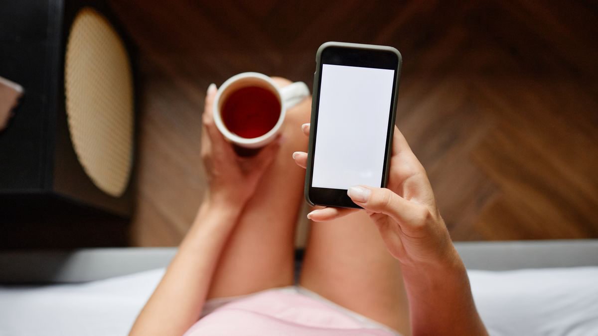 Woman checking her smartphone while holding a cup of coffee